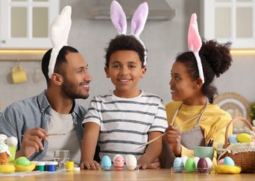 Happy African American family painting Easter eggs at table in kitchen