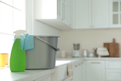 Detergent and plastic bucket with rag on countertop in kitchen, space for text. Cleaning supplies