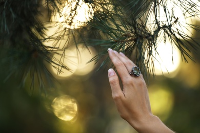 Photo of Young woman wearing beautiful silver ring with prehnite gemstone near pine, closeup. Space for text