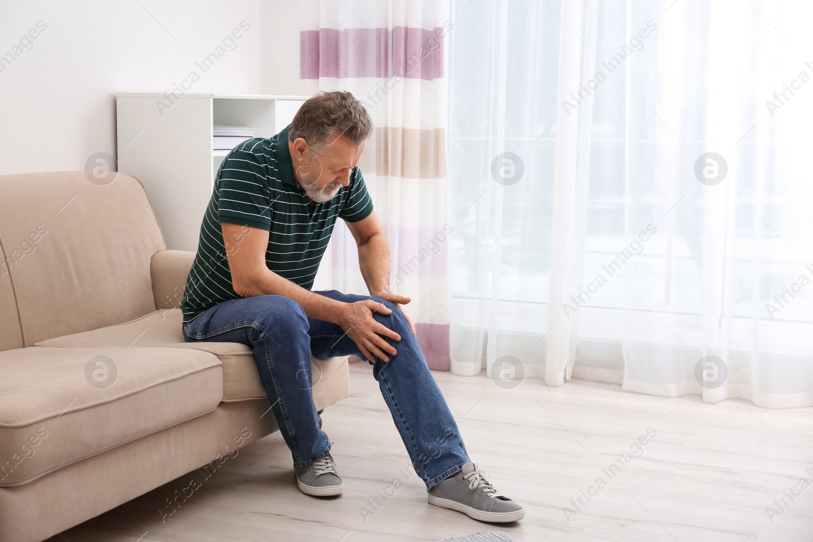 Photo of Senior man suffering from knee pain at home. Space for text