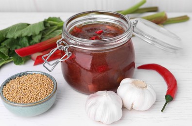 Tasty rhubarb sauce and ingredients on white wooden table