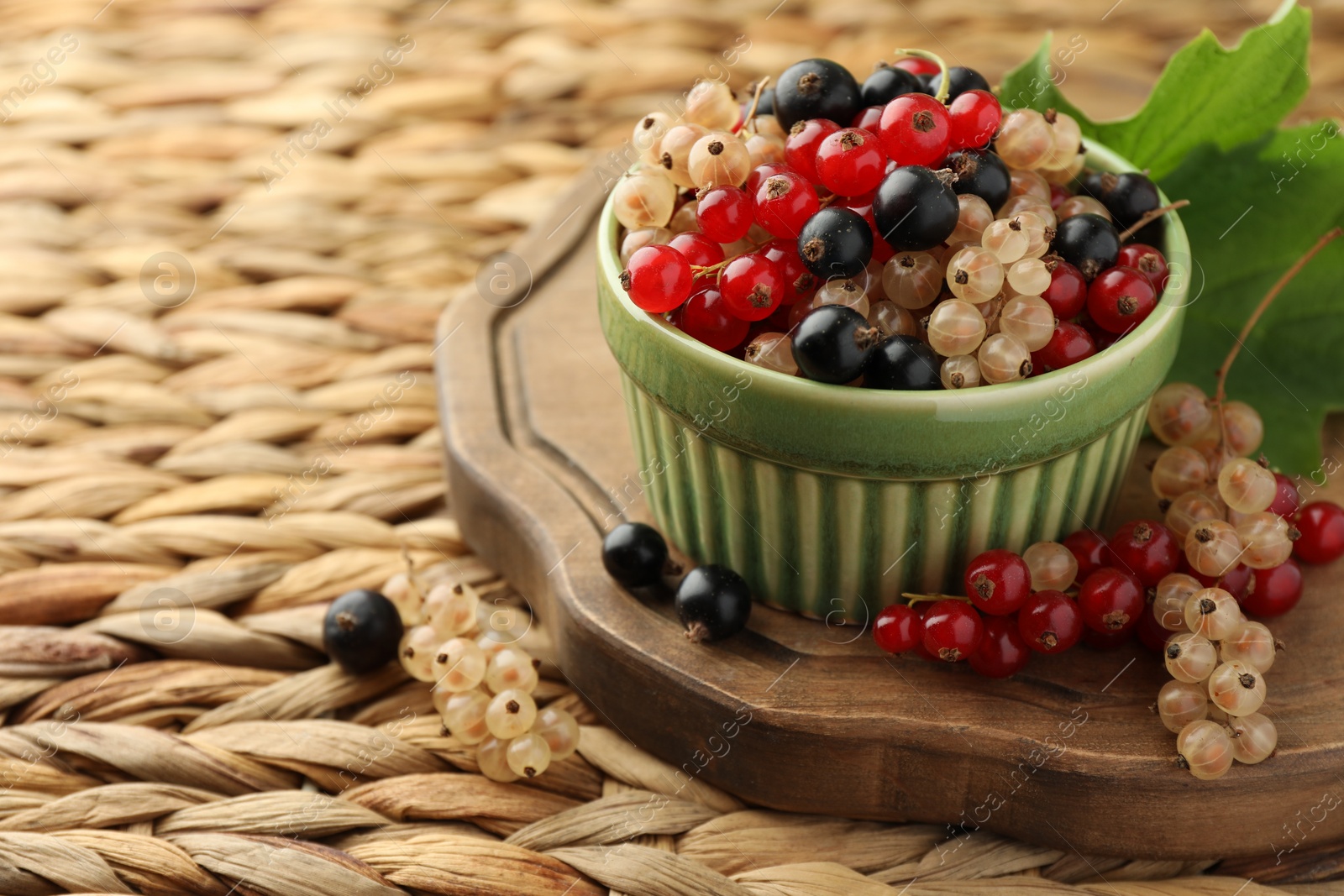 Photo of Different fresh ripe currants and green leaf on wicker surface, space for text