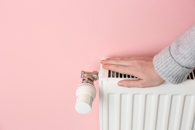Photo of Woman warming hand on heating radiator against color background