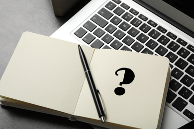 Photo of Notebook with question mark, pen and laptop on grey table, closeup