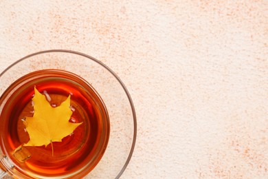 Cup of tasty tea and autumn yellow leaf on color background, top view. Space for text