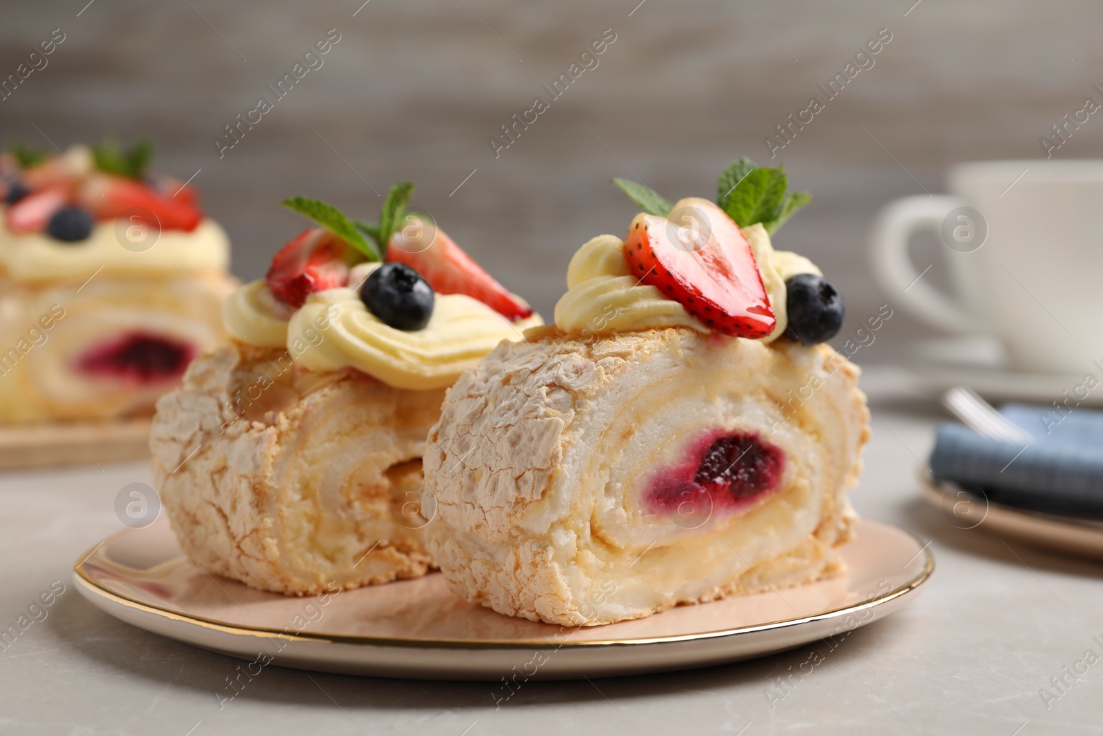 Photo of Pieces of tasty meringue roll with jam, cream, strawberry, blueberry and mint on light grey marble table, closeup