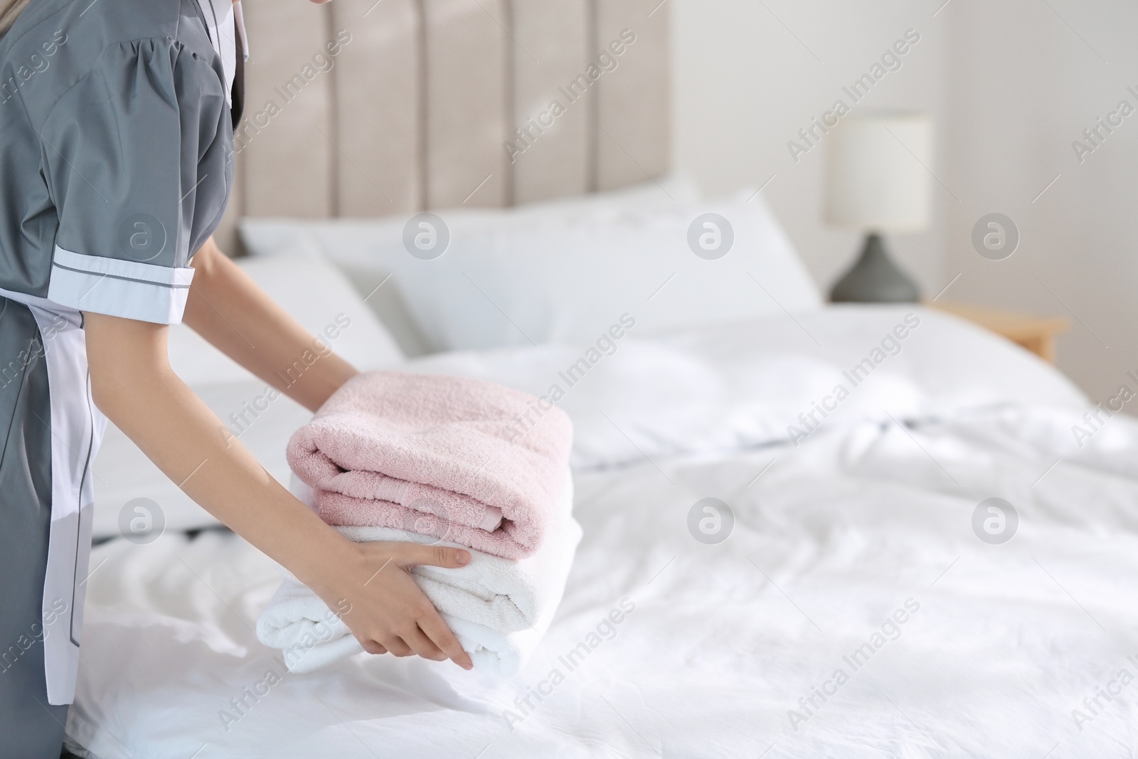 Photo of Young chambermaid putting stack of fresh towels on bed in hotel room, closeup. Space for text