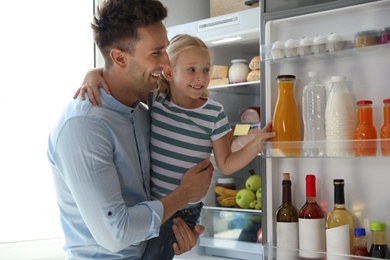 Father and daughter taking bottle with juice out of refrigerator in kitchen