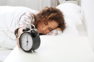 Photo of Young African-American woman turning off alarm clock at home. Bedtime