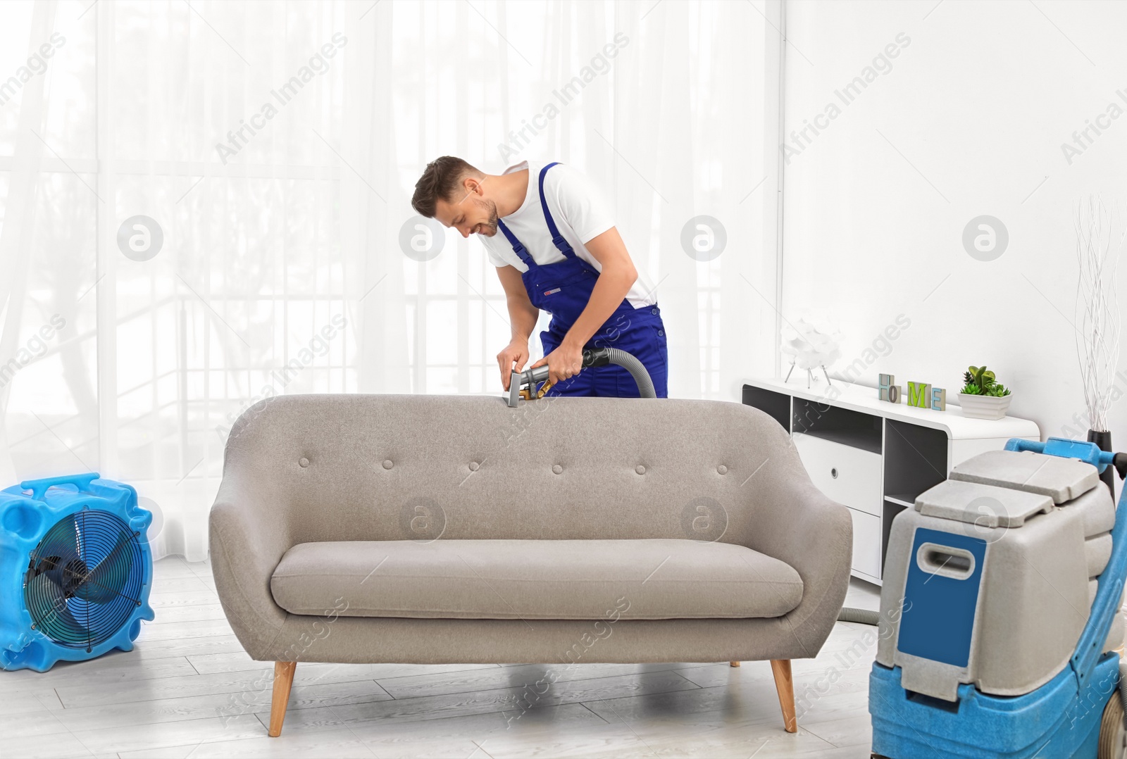 Photo of Dry cleaning worker removing dirt from sofa indoors