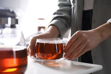 Woman with cup of hot tea at white table, closeup