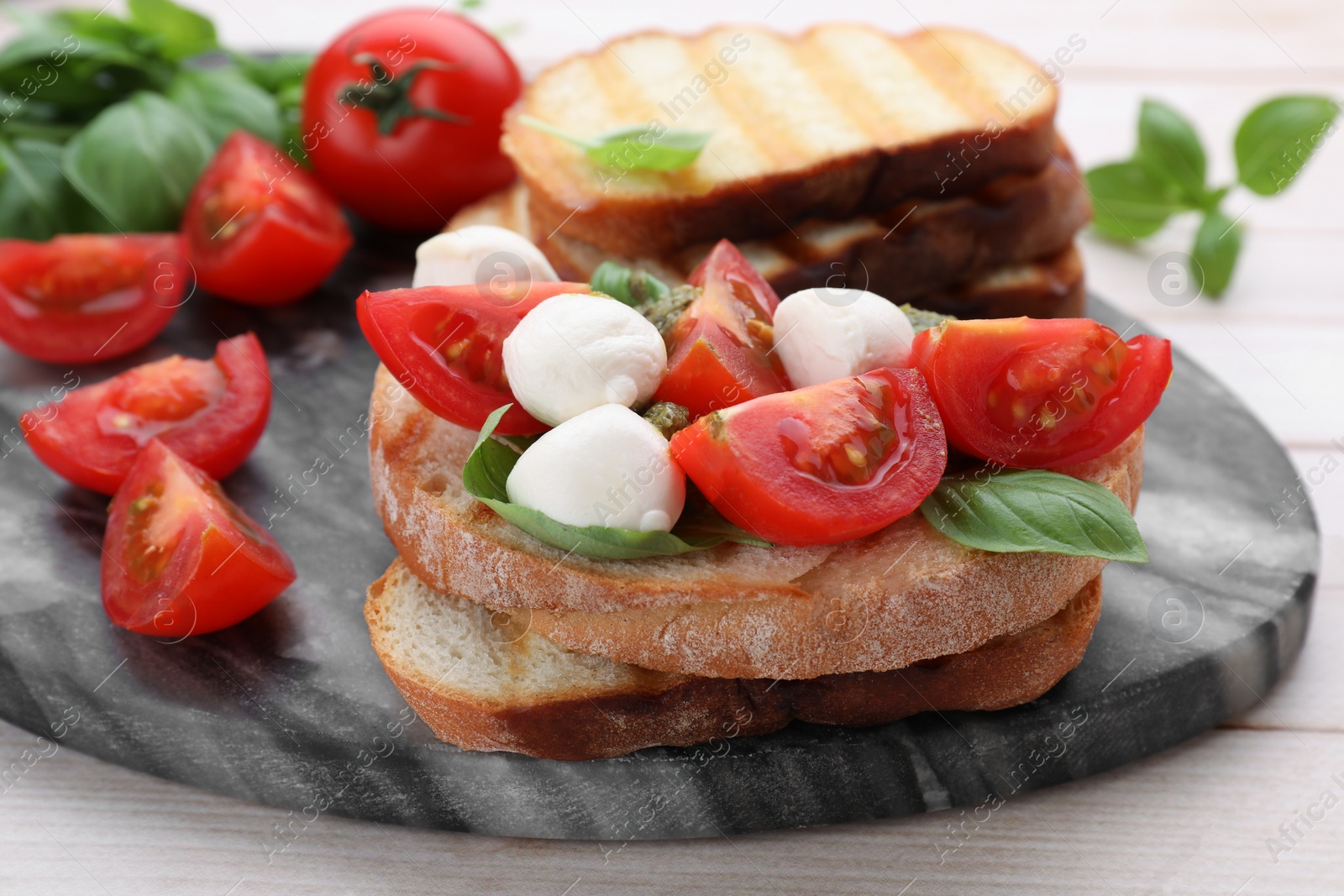 Photo of Delicious Caprese sandwich with mozzarella, tomatoes, basil and pesto sauce on white wooden table, closeup