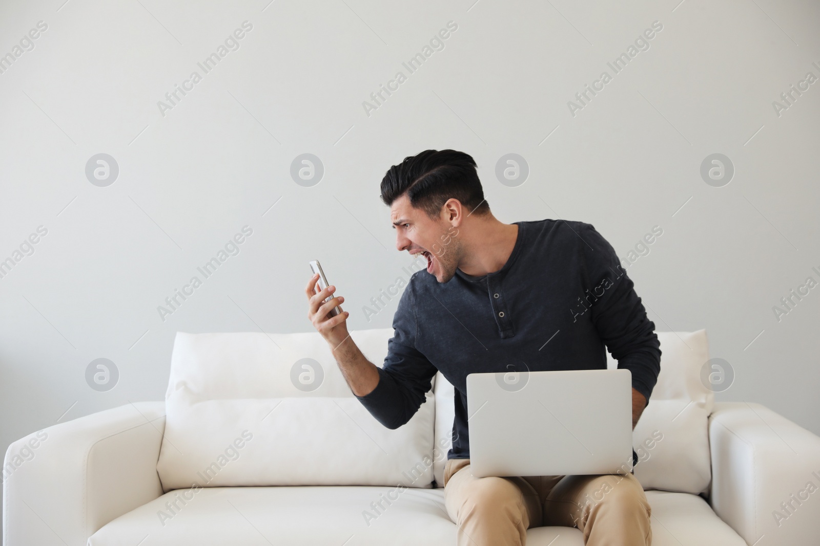 Photo of Emotional man with smartphone and laptop at home