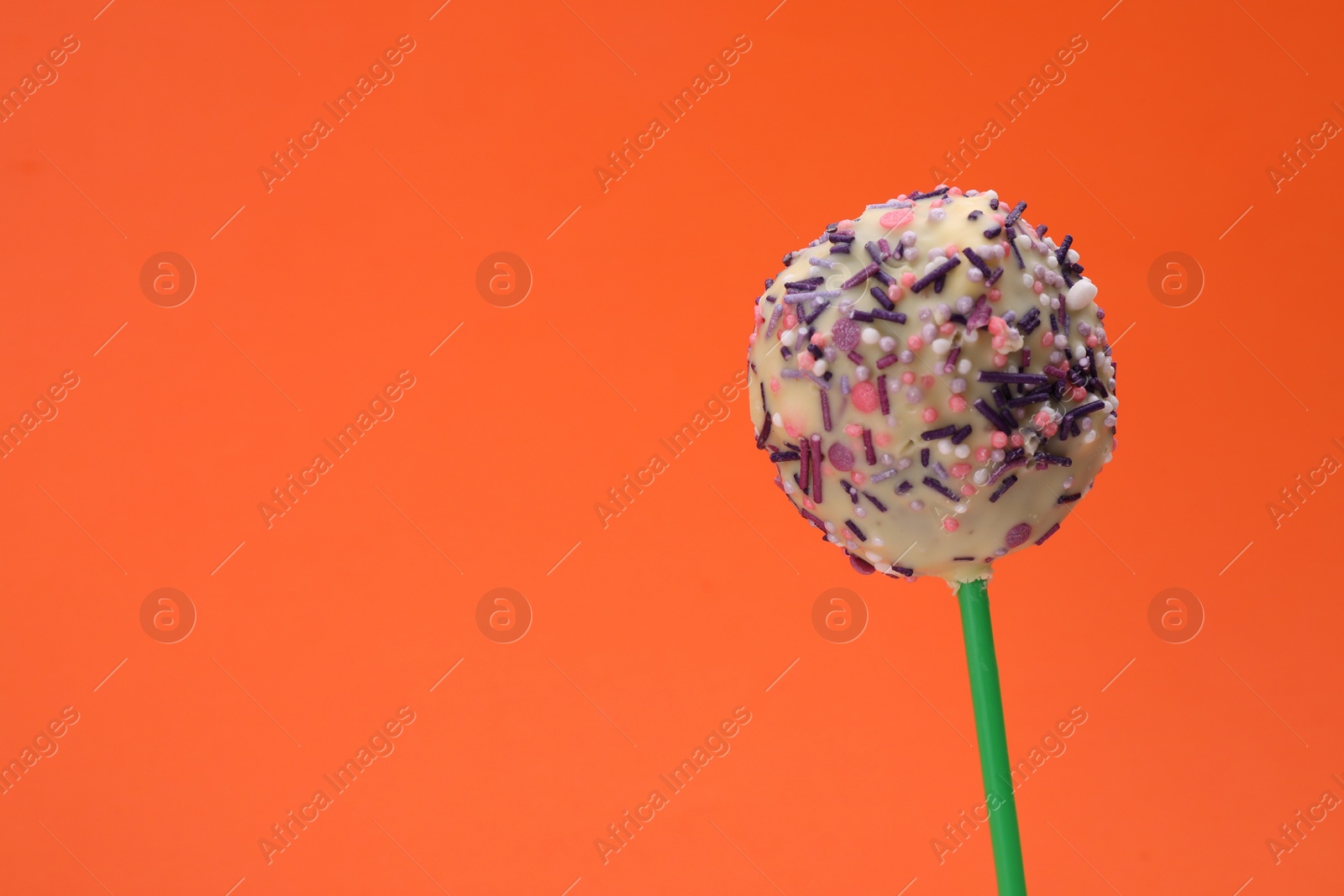 Photo of Delicious confectionery. Sweet cake pop decorated with sprinkles on orange background, closeup. Space for text