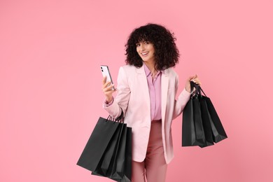 Photo of Happy young woman with shopping bags and modern smartphone on pink background. Space for text