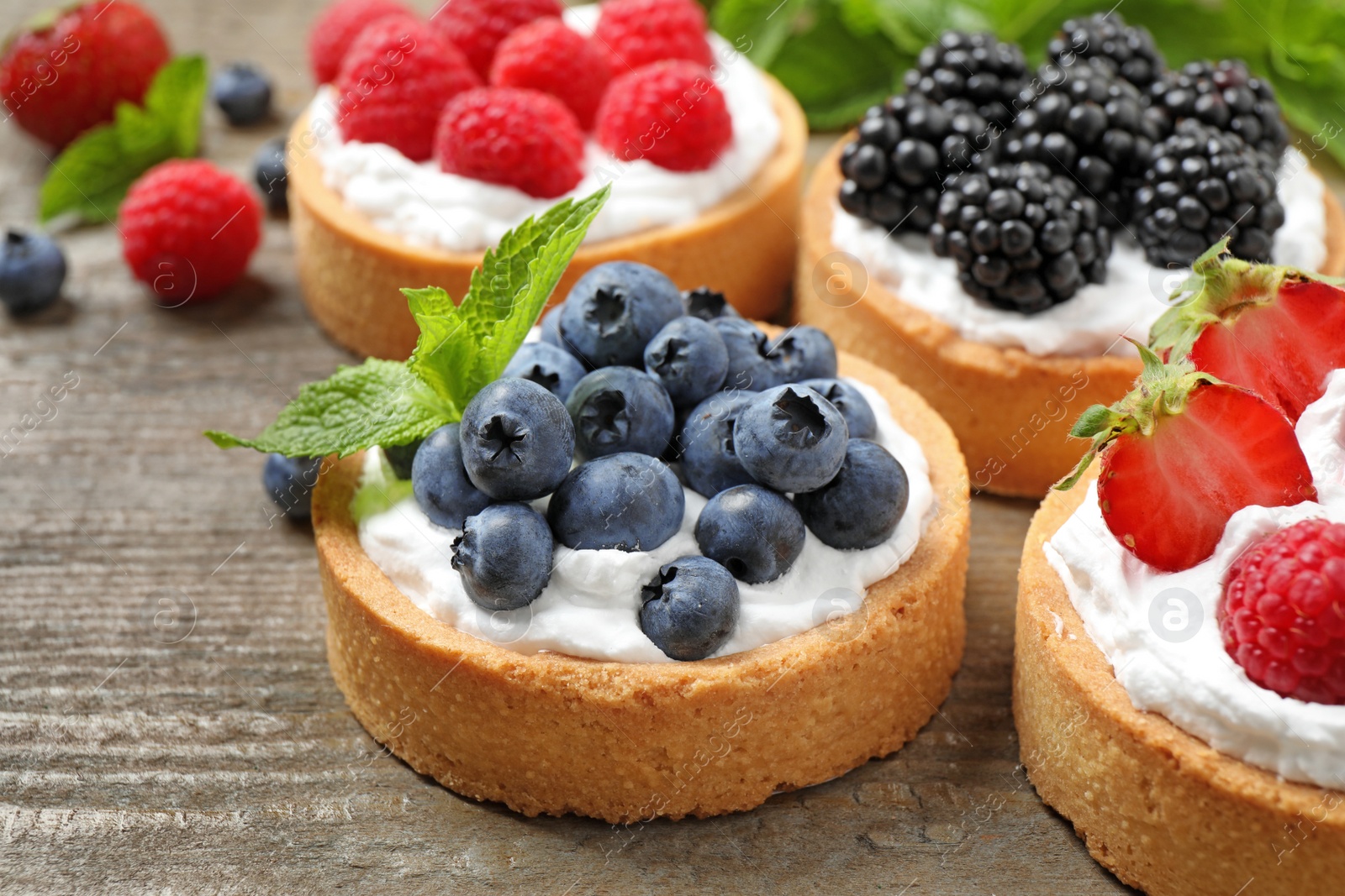 Photo of Different berry tarts on wooden table, closeup. Delicious pastries