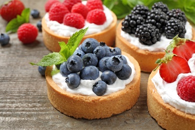 Photo of Different berry tarts on wooden table, closeup. Delicious pastries