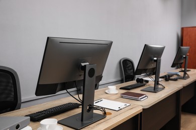 Photo of Open office interior. Modern workplaces with computers near light grey wall