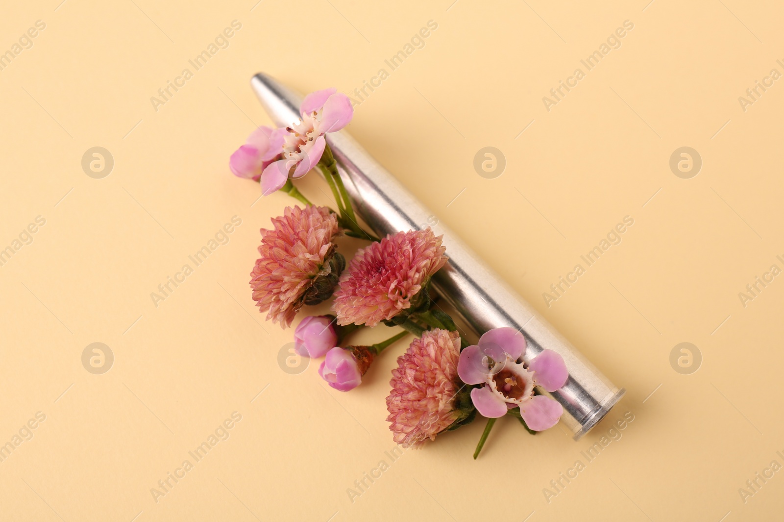 Photo of One metal bullet and beautiful flowers on yellow background, closeup