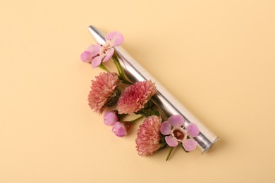 Photo of One metal bullet and beautiful flowers on yellow background, closeup