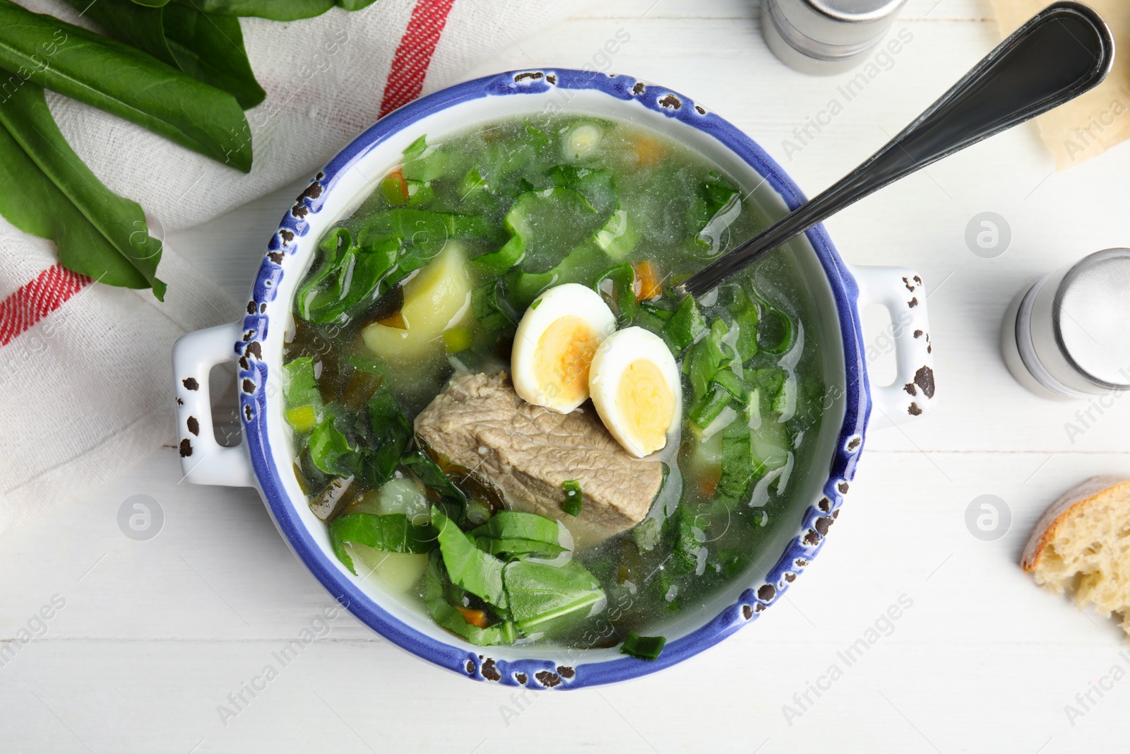 Photo of Delicious sorrel soup with meat and eggs served on white wooden table, flat lay