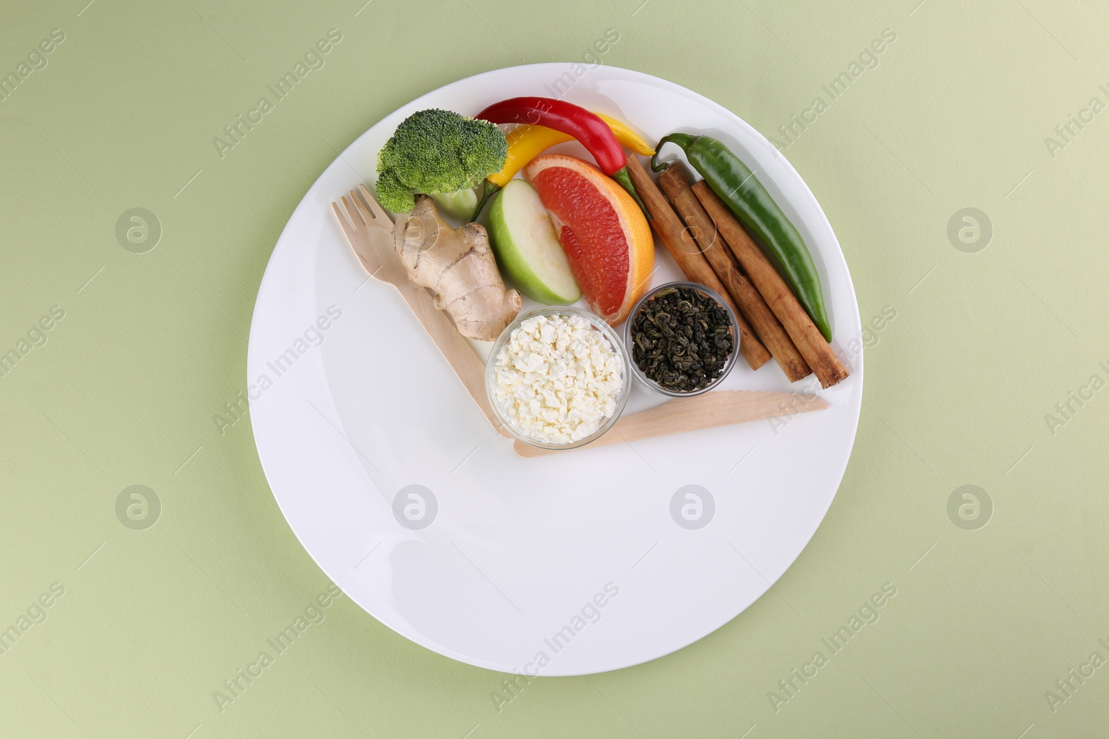 Photo of Metabolism. Plate with different food products and wooden cutlery on pale green background, top view