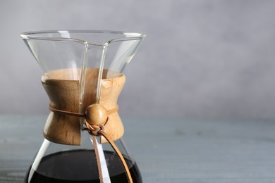 Photo of Glass chemex coffeemaker with tasty drip coffee on table against grey background, closeup. Space for text