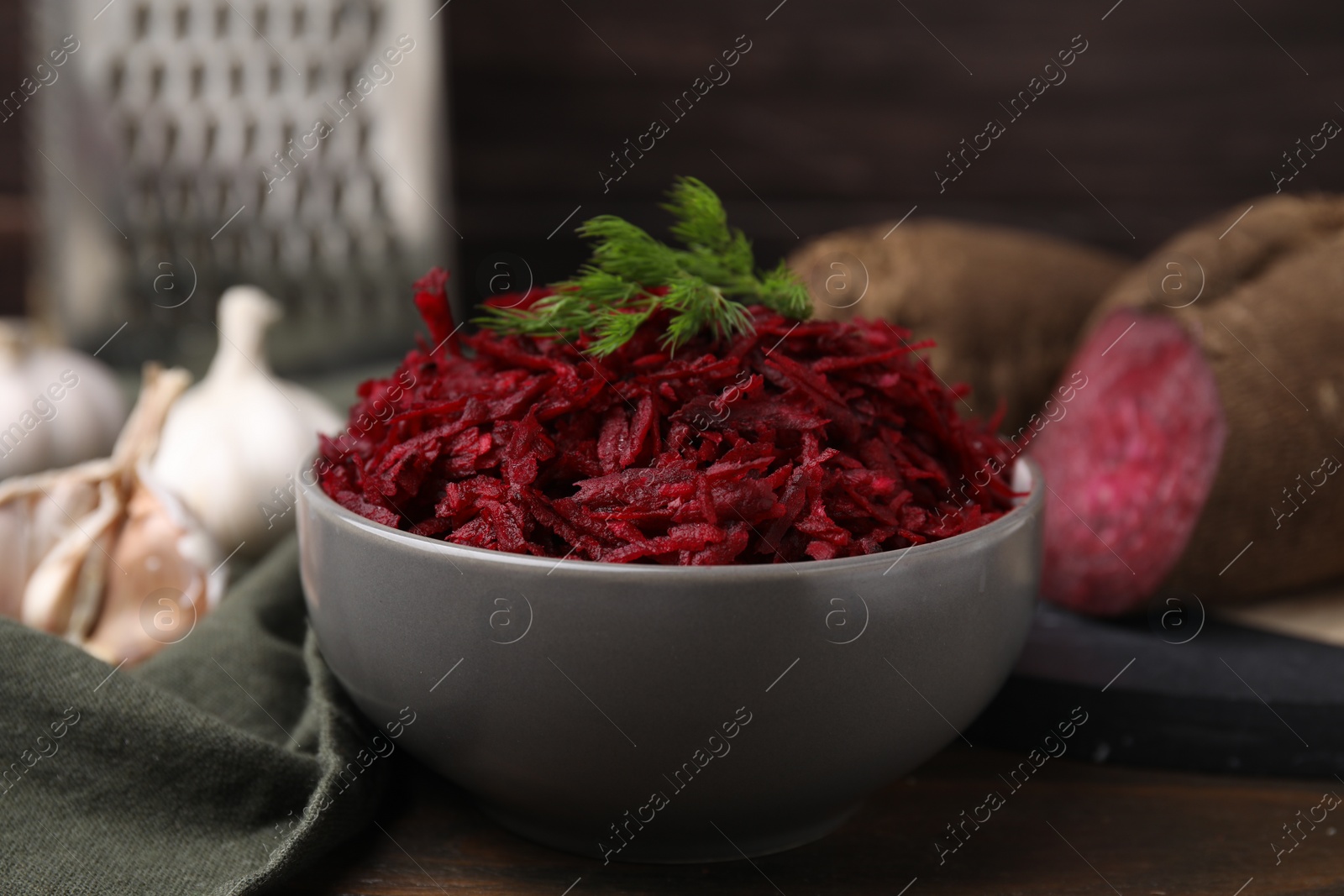 Photo of Grated red beet and dill in bowl on table, closeup