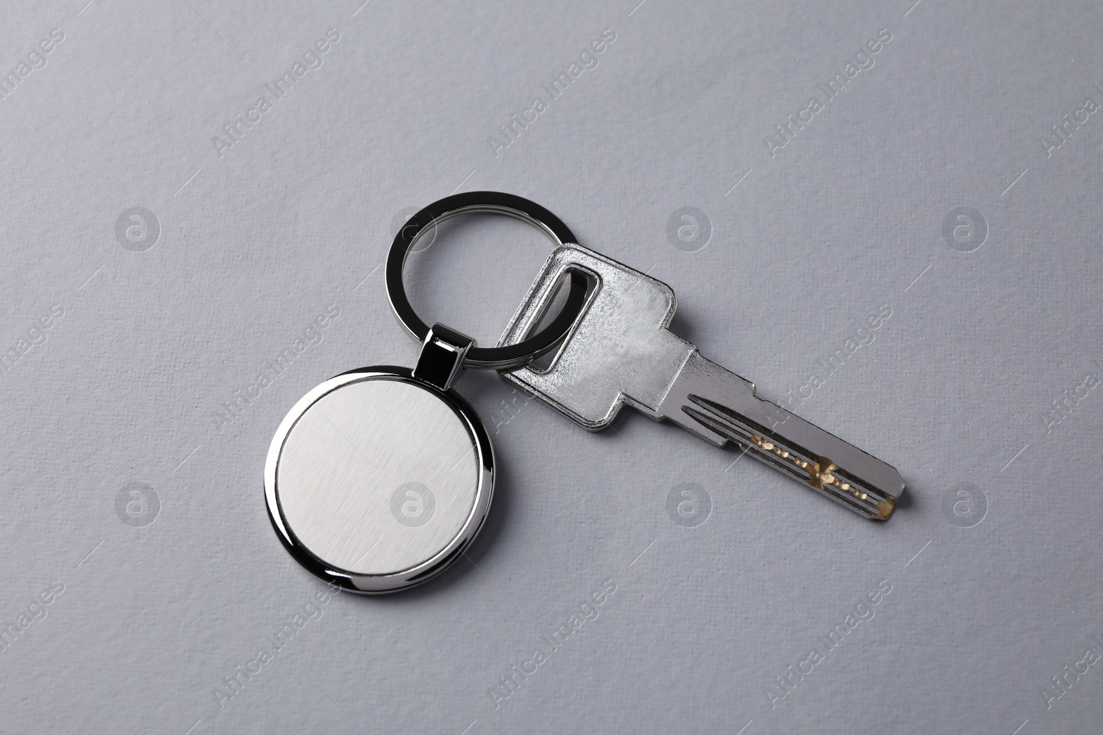 Photo of Key with metallic keychain on light grey background, top view