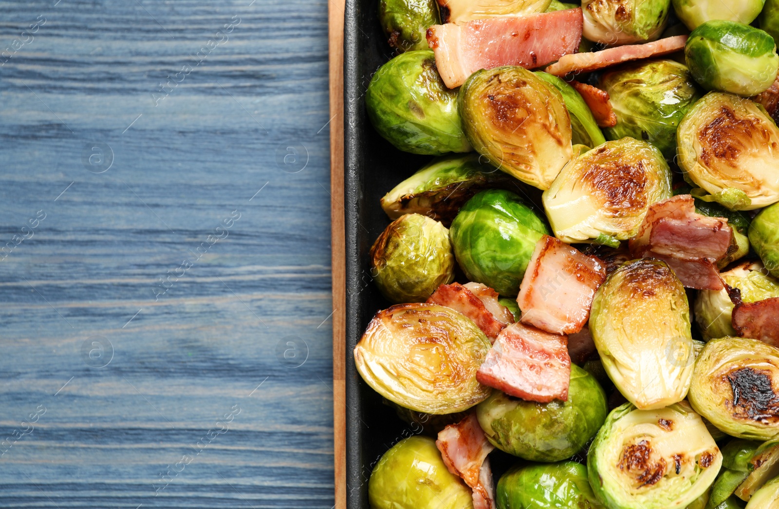 Photo of Delicious Brussels sprouts with bacon in baking pan on blue wooden table, top view