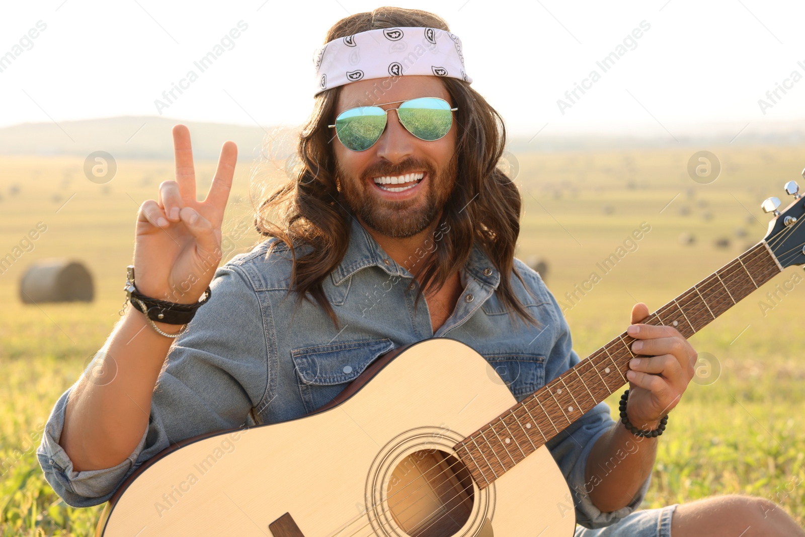 Photo of Happy hippie man with guitar showing peace sign in field