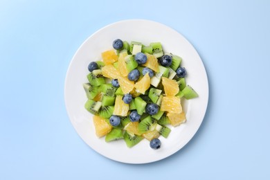 Photo of Plate of tasty fruit salad on light blue background, top view