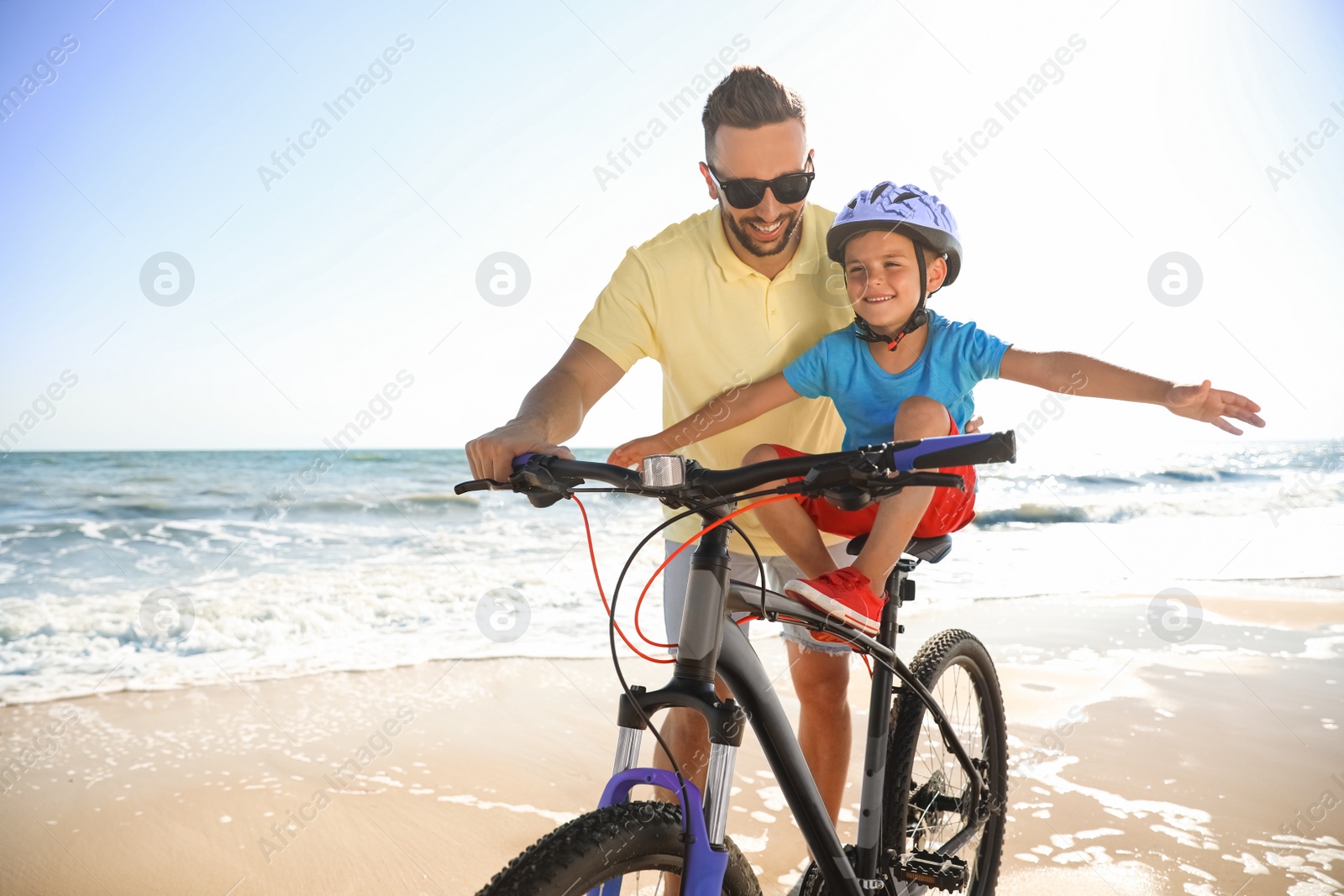 Photo of Happy father teaching son to ride bicycle on sandy beach near sea