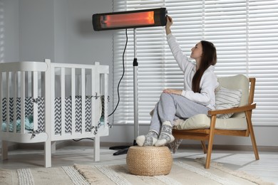 Photo of Young woman adjusting temperature on modern electric infrared heater in child room