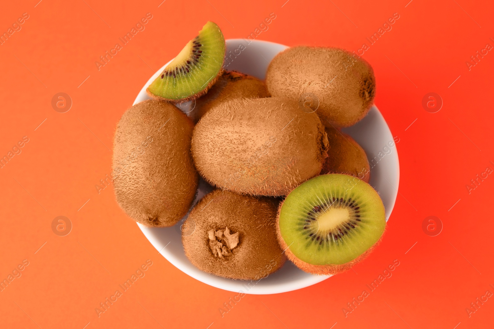 Photo of Bowl of whole and cut fresh ripe kiwis on orange background, top view