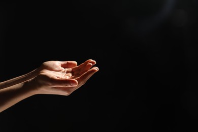 Religion. Woman with open palms praying on black background, closeup. Space for text