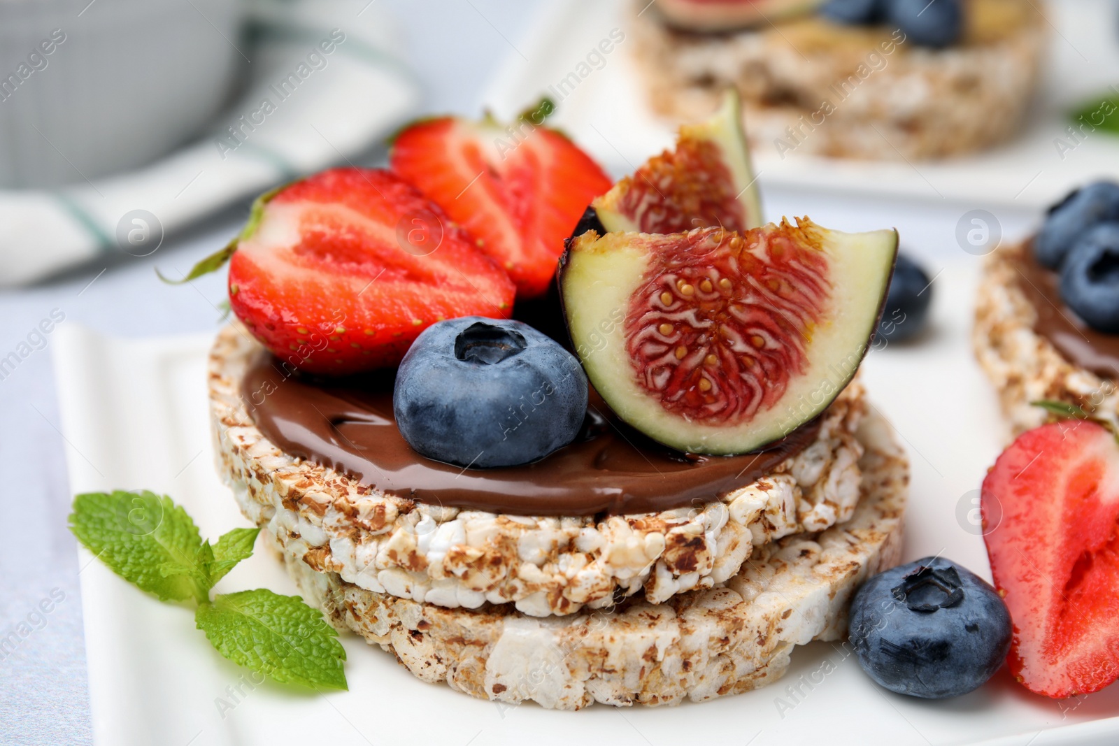 Photo of Tasty crispbreads with chocolate, figs and berries served on light table, closeup