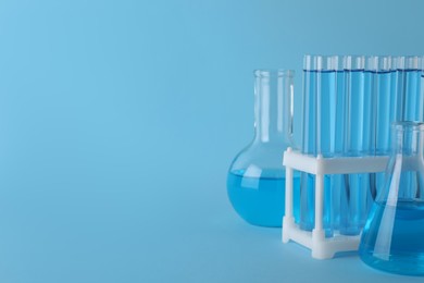 Photo of Laboratory glassware with light blue liquid on turquoise background. Space for text