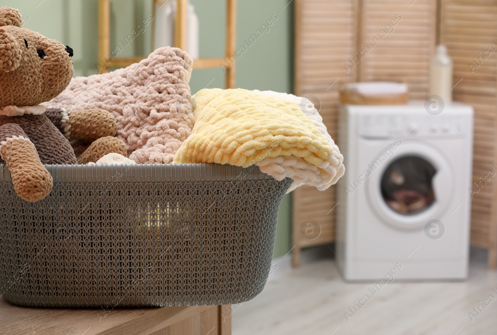 Photo of Laundry basket with soft blankets and toy in bathroom, closeup. Space for text