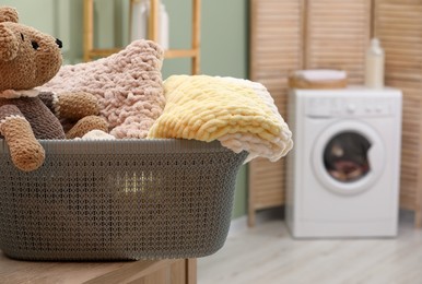 Photo of Laundry basket with soft blankets and toy in bathroom, closeup. Space for text
