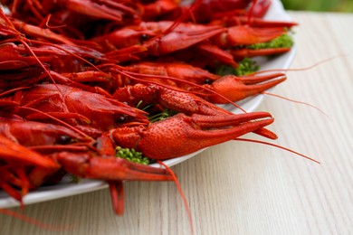 Plate with delicious red boiled crayfish on white wooden table, closeup