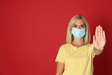 Woman in protective mask showing stop gesture on red background, space for text. Prevent spreading of coronavirus