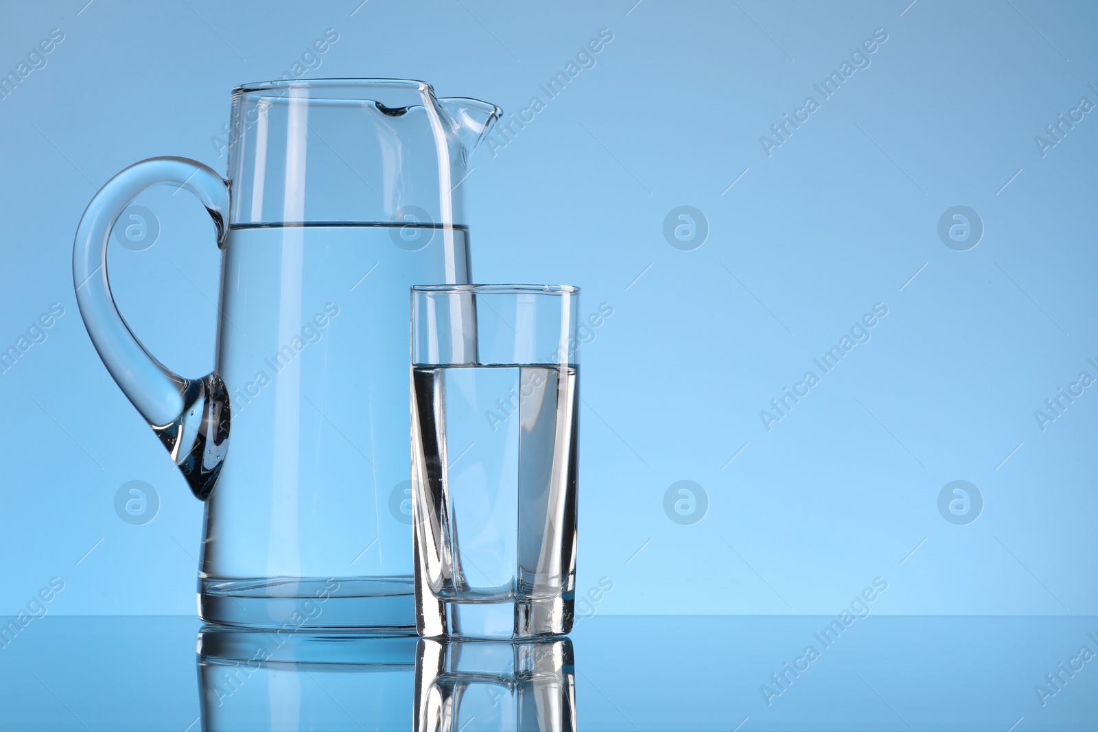 Photo of Glass and jug with water on light blue background. Space for text