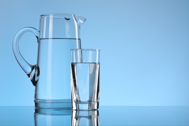 Photo of Glass and jug with water on light blue background. Space for text