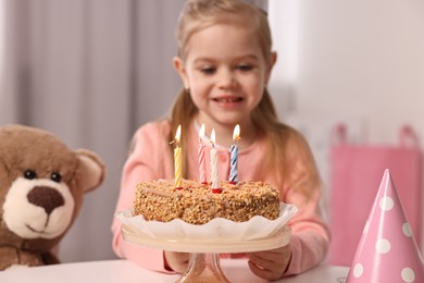 Cute girl with birthday cake at table indoors, focus on burning candles