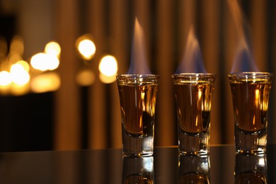 Photo of Flaming alcohol drink in shot glasses on mirror surface against blurred background, closeup. Space for text