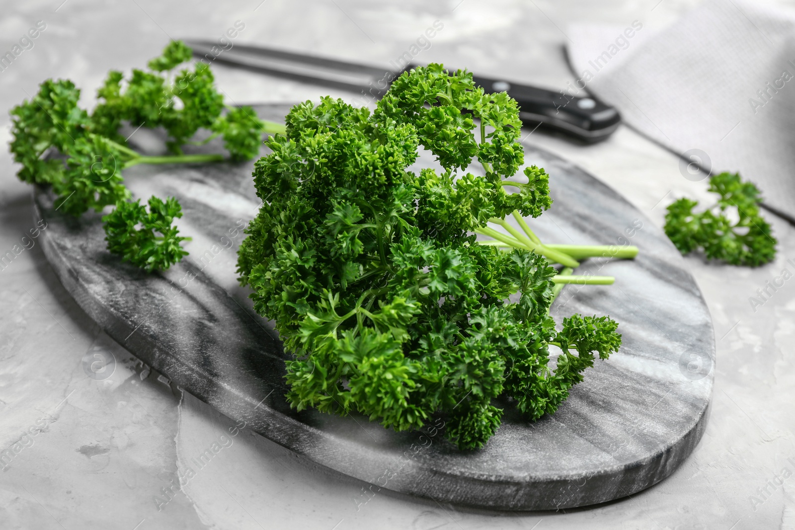 Photo of Fresh curly parsley and cutting board on grey table