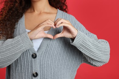 Photo of African-American woman making heart with hands on red background, closeup