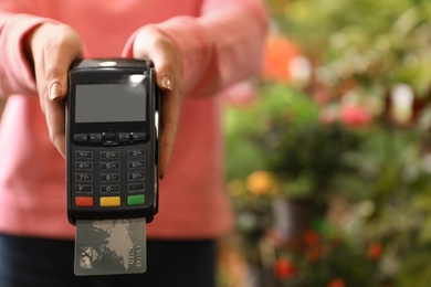 Seller holding payment terminal with credit card on blurred background, closeup. Space for text