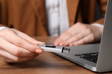 Photo of Woman holding usb flash drive near laptop at wooden table, closeup